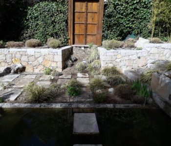 rocaille_au_bord_de_point_eau_et_massifs_fraichement_tailles_dvant_une_belle_porte_en_bois_et_une_haie_tailee